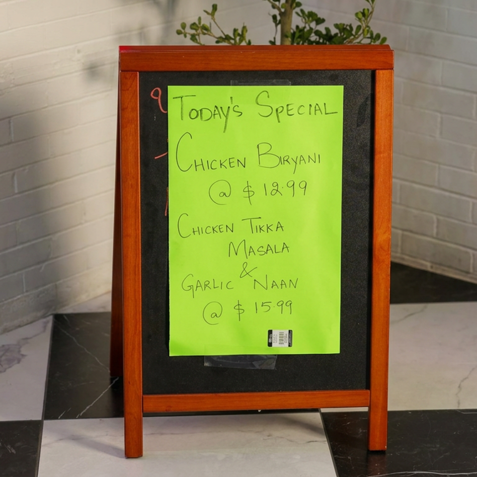 Chalkboard restaurant sign advertises chicken biryani, chicken tikka masala, and garlic naan specials with prices.